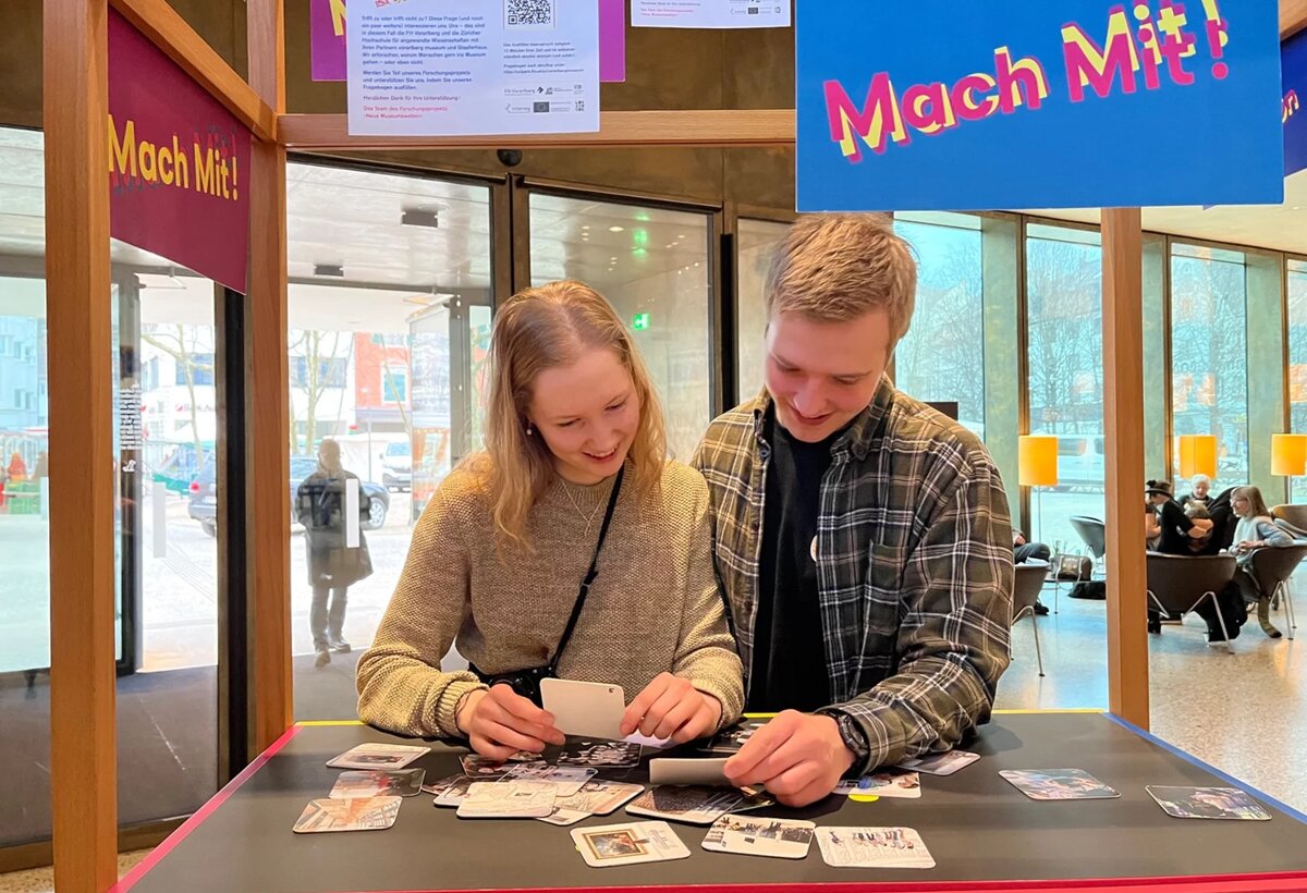 Zwei Personen stehen an einem Stand und sotieren Karten | © FHV