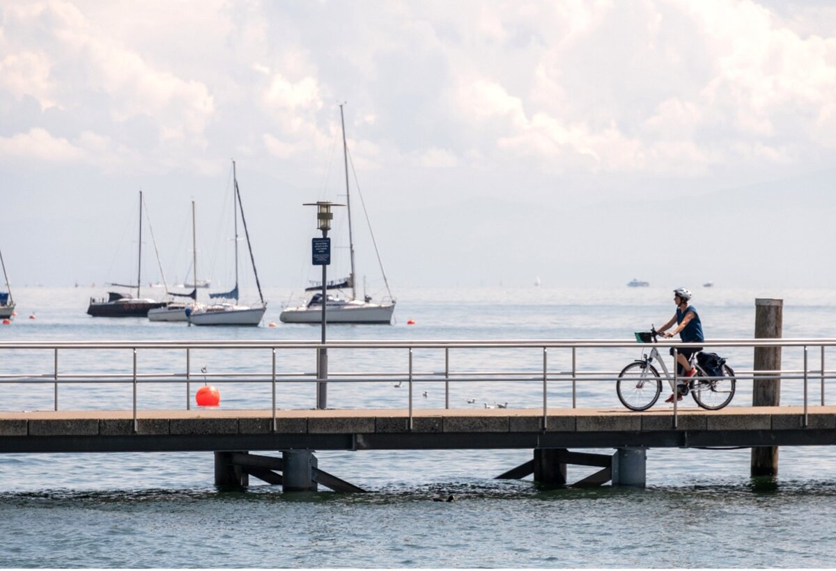 Naturerlebnis am Bodensee mit dem Fahrrad, Frau fährt mit Elektro-Fahrrad auf Bootssteg, weiter Blick auf Bodensee | © Adobe Stock