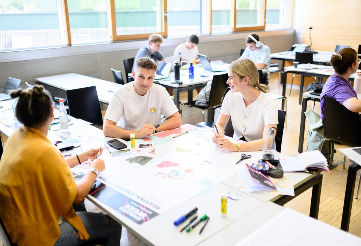 Studierende sitzen an einem Tisch und stellen auf einem Poster ihre Ideen für ein ein nachhaltiges Energiesystem für Vorarlberg dar. | © FHV/Matthias Rhomberg