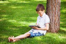 HCT-Anwendung: Wohlfühltagebuch | © FHV Ein Junge sitzt im Gras und lehnt an einem Baum. Er hat ein Tablet in der Hand. | © FHV