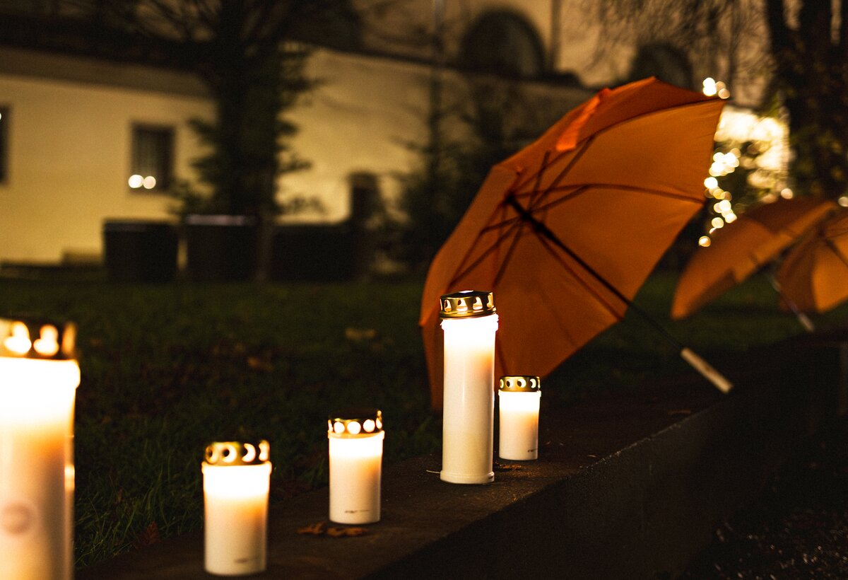 Brennende Kerzen und ein oranger Regenschirm im Hintergrund | © FHV